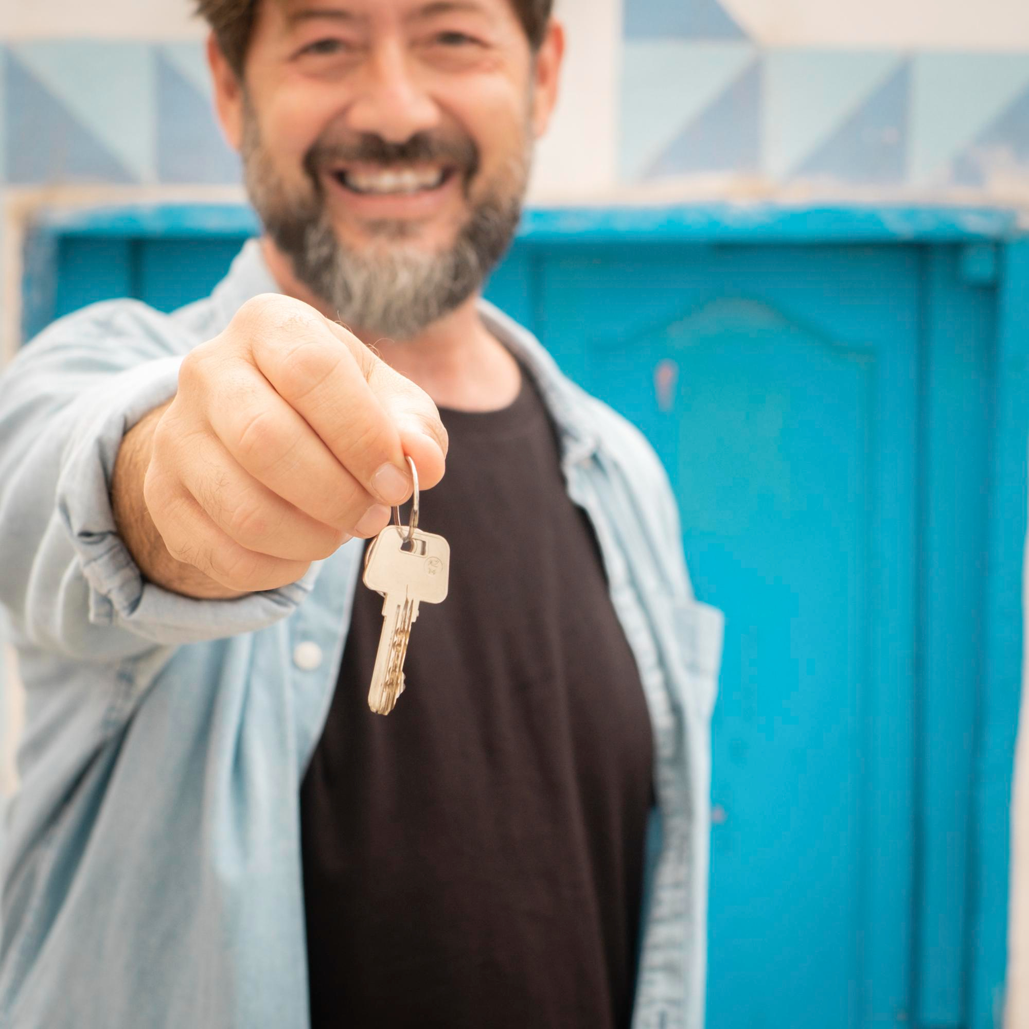 adult happy man holding home keys blue door house background concept buyer properties bank loan mortgage moving cheerful people renting apartment showing keys